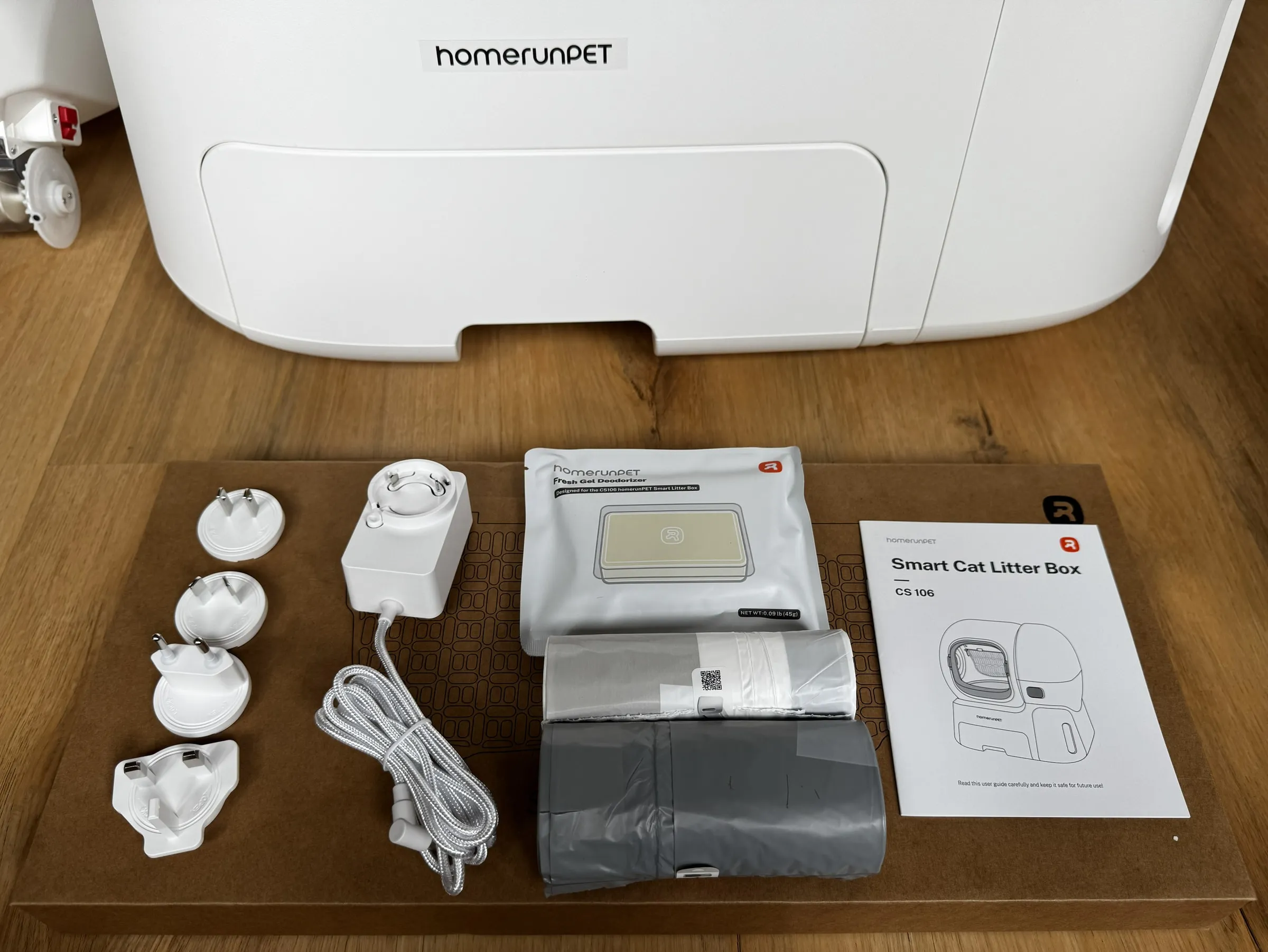 Included homerunPET CS106 accessories laid out in front of the litter box, including bags, gel, adapter, and quick start guide
